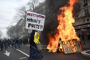 Un protestataire tient une pancarte portant l’inscription « destitution » à côté de cagettes en feu lors d’une manifestation à Paris contre la réforme des retraites, adoptée grâce au 49.3, le 23 mars 2023.