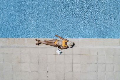 Jeune femme allongée sur le bord d'une piscine, en maillot de bain, avec un chapeau, au soleil, Provence, France.